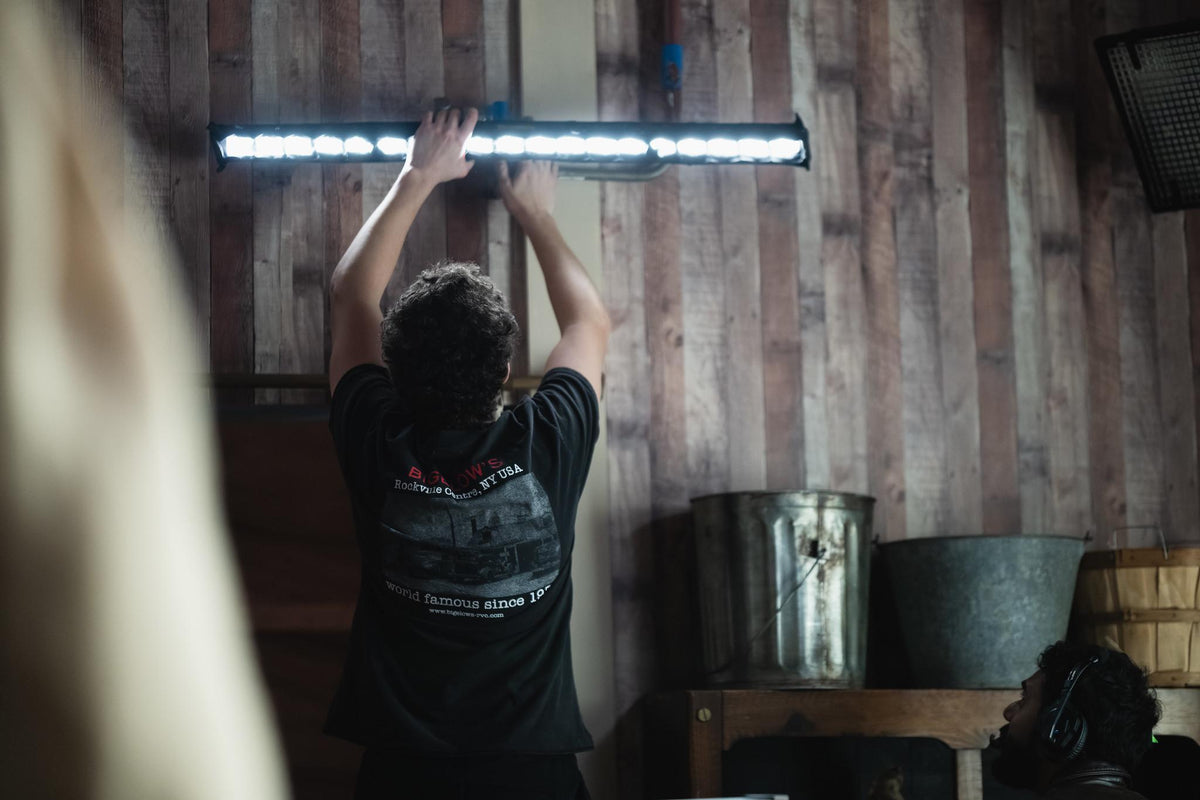A crew member adjusting a light in a wood-paneled room.